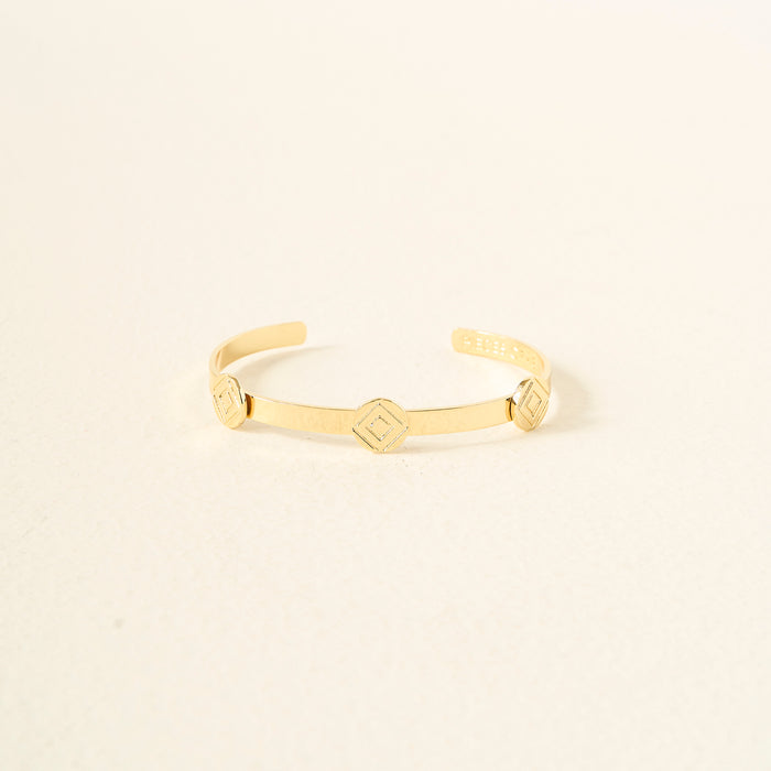 The Darling Effect’s You Are Determined Skinny Stacker Bracelet is a minimal 14k gold-plated adjustable cuff with three small hexagonal accents—gift-ready jewelry displayed on a chic, textured surface.