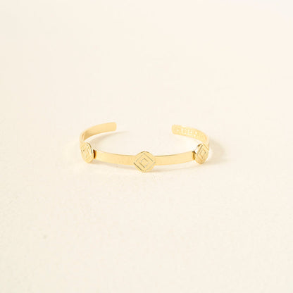 The Darling Effect’s You Are Determined Skinny Stacker Bracelet is a minimal 14k gold-plated adjustable cuff with three small hexagonal accents—gift-ready jewelry displayed on a chic, textured surface.