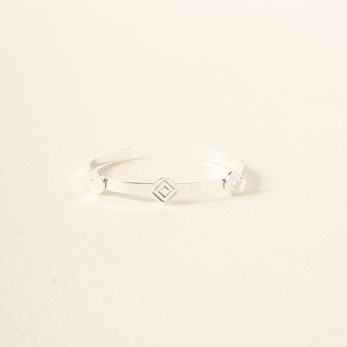 The Darling Effect’s "You Are Determined" Skinny Stacker Bracelet is a polished silver adjustable cuff with three diamond-shaped charms, shown on a cream background—an elegant, gift-ready accessory.