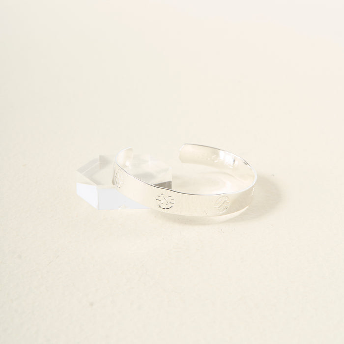 The Darling Effect’s You Are Driven Cuff Bracelet, crafted in sterling silver with embossed circular designs and text, is displayed on a clear acrylic stand against a light background—a meaningful and elegant gift.