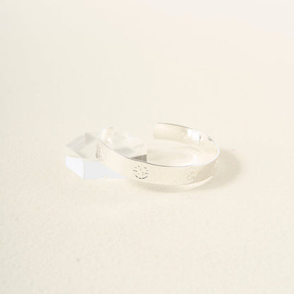 The Darling Effect’s You Are Driven Cuff Bracelet, crafted in sterling silver with embossed circular designs and text, is displayed on a clear acrylic stand against a light background—a meaningful and elegant gift.
