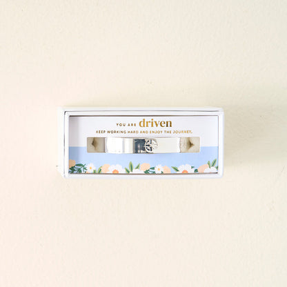 The Darling Effect's You Are Driven Cuff Bracelet is a sterling silver piece inscribed with "YOU ARE driven. KEEP WORKING HARD AND ENJOY THE JOURNEY," presented in a floral-bordered gift box—a meaningful gift.