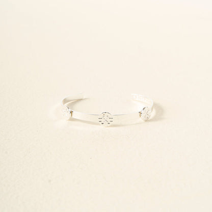 The Darling Effect’s You Are Driven Skinny Stacker Bracelet is an adjustable silver cuff with three engraved circular floral designs, displayed on a light cream background.