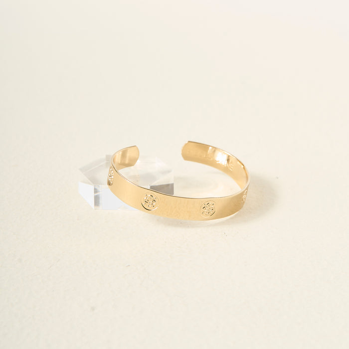 The Darling Effect’s You Are Friendly Trait Cuff Bracelet, featuring embossed circular designs, sits on a clear acrylic block against a light beige background—a thoughtful gift for any occasion.