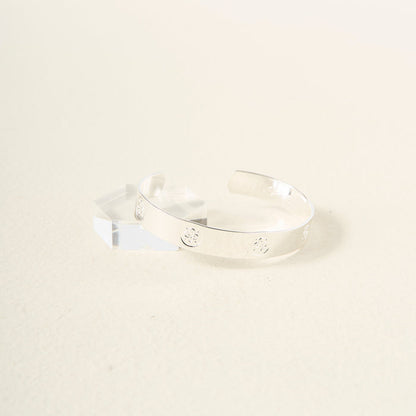 The Darling Effect’s You Are Friendly Trait Cuff Bracelet, crafted in sterling silver with small circular engravings, is shown on a light surface beside a clear geometric acrylic block—an ideal gift for any occasion.