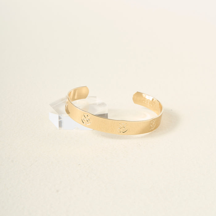 The Darling Effect's "You Are Hard-Working" cuff bracelet, featuring engraved floral designs in gold, rests on a clear acrylic block against a soft beige background—an elegant and thoughtful gift.