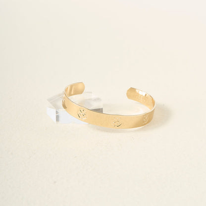 The Darling Effect's "You Are Hard-Working" cuff bracelet, featuring engraved floral designs in gold, rests on a clear acrylic block against a soft beige background—an elegant and thoughtful gift.
