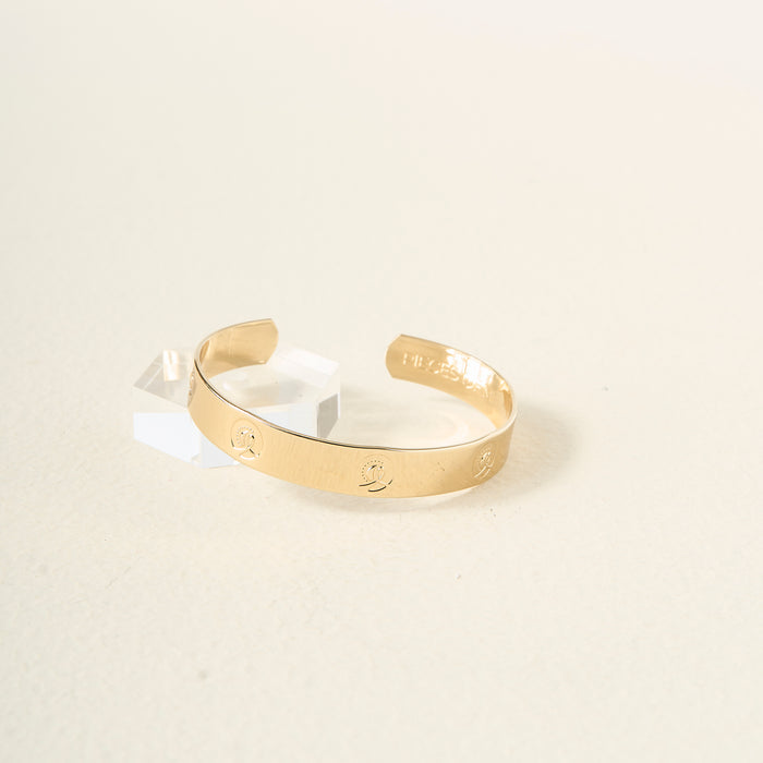 The Darling Effect's You Are Independent Cuff Bracelet, featuring engraved designs and an adjustable fit, rests elegantly on a light surface beside a small clear acrylic block.