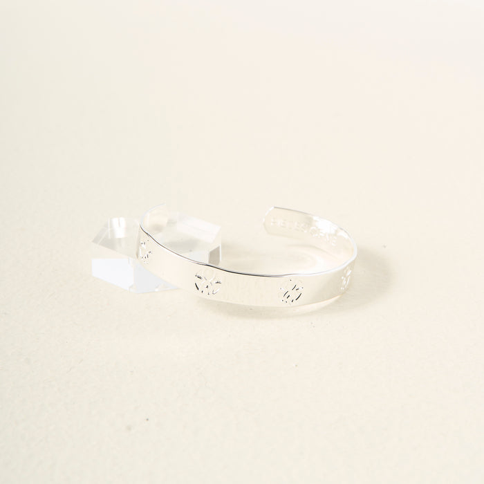 The Darling Effect’s You Are Loyal Cuff Bracelet, made of sterling silver with cut-out geometric designs, is shown adjustable beside a clear acrylic block on a neutral background, blending modern style with timeless elegance.