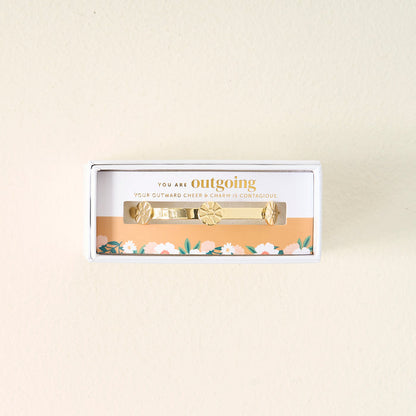 Gift-ready from The Darling Effect, the You Are Outgoing Skinny Stacker Bracelet is a 14k gold plated adjustable cuff in a box, delicately accented with florals and engraved: YOU ARE outgoing. YOUR OUTWARD CHEER & CHARM IS CONTAGIOUS.