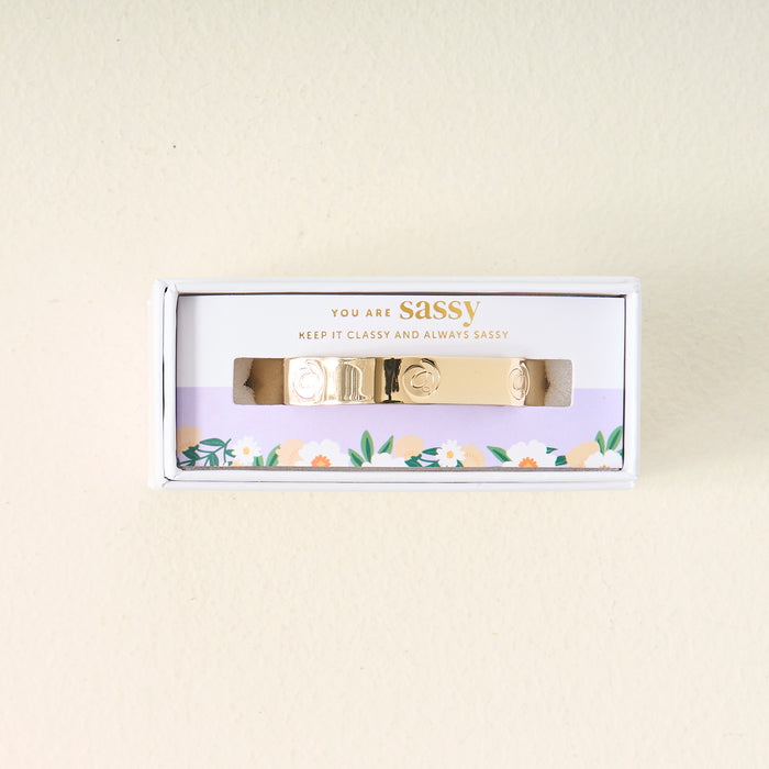 The Darling Effect's You Are Sassy Cuff Bracelet, featuring engraved designs, comes in a white box with a floral border. The packaging says "YOU ARE SASSY" and "KEEP IT CLASSY AND ALWAYS SASSY.