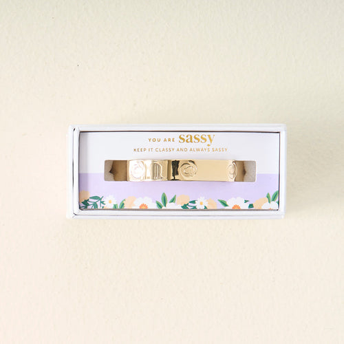 The Darling Effect's You Are Sassy Cuff Bracelet, featuring engraved designs, comes in a white box with a floral border. The packaging says "YOU ARE SASSY" and "KEEP IT CLASSY AND ALWAYS SASSY.