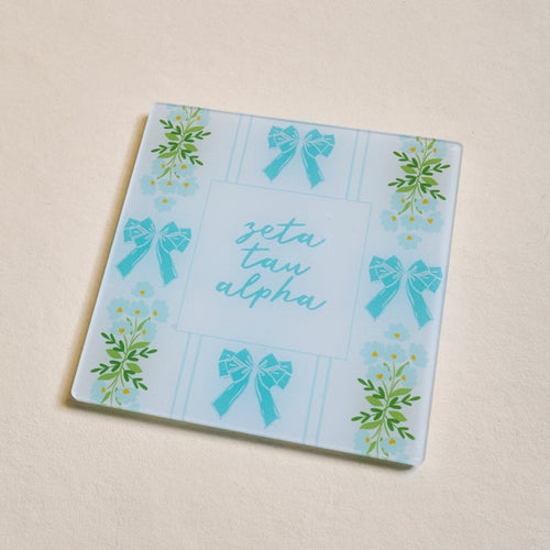 The Darling Effect’s Zeta Tau Alpha Acrylic Coaster features a light blue background with blue bows, green florals, and “zeta tau alpha” in cursive—perfect for showcasing your sorority pride or gifting to a fellow sister.